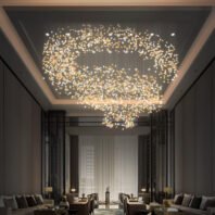 A stunning large chandelier dominates a hotel lounge, featuring custom lighting that resembles a swirling galaxy. This big chandelier, composed of thousands of golden and white illuminated elements, creates a mesmerizing spiral pattern. The hotel chandelier floats within a dark recessed ceiling, its organic design mirroring a celestial formation. Below, an elegant seating area showcases the chandelier's warm glow, emphasizing how custom lighting can transform spaces into captivating, luxurious environments.