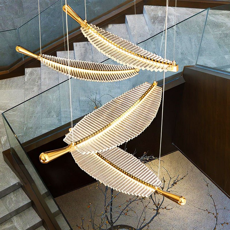 A stunning custom lighting installation featuring multiple feather-like chandeliers suspended in a modern stairwell. Each chandelier consists of illuminated white glass rods arranged along a curved gold support, resembling elongated feathers or leaves. The fixtures are suspended at various angles, creating a dynamic, floating effect that complements the angular lines of the staircase. The staircase itself is made of gray stone or concrete, with glass balustrades adding to the contemporary feel. At the bottom of the image, decorative branches are visible, adding an organic touch to the sleek, modern design. The interplay of light from the chandeliers creates a warm, inviting atmosphere in the stairwell, transforming a functional space into an artistic focal point. This bespoke lighting design beautifully merges form and function, elevating the entire architectural space.