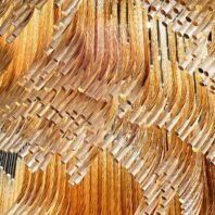 A close-up view of an extraordinary large chandelier showcasing innovative custom lighting design for luxury hotels. This big chandelier features hundreds of curved, translucent glass tubes in varying shades of amber and gold, creating a mesmerizing wave-like effect. The hotel chandelier's unique composition resembles a flowing golden river or a field of wheat swaying in the breeze. Each glass element is carefully arranged to form fluid, organic patterns that catch and reflect light. The intricate layering of the glass tubes adds depth and dimension to the piece. This exquisite custom lighting installation transforms any space into a striking, artistic display, perfect for creating a warm, sophisticated atmosphere in high-end hospitality environments such as upscale hotel lobbies or grand ballrooms.