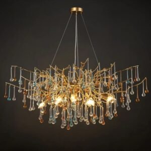 An opulent chandelier featuring an intricate gold-toned branch structure adorned with numerous crystal droplets in various colors. The fixture has an organic, tree-like design with golden branches extending outward and downward in a graceful, asymmetrical pattern. Hanging from these branches are crystal pendants in clear, light blue, and amber hues, creating a multi-colored sparkling effect. The chandelier is illuminated from within, with visible warm light bulbs nestled among the golden branches, casting a soft glow through the crystals. The fixture is suspended from a circular gold ceiling mount by thin wires. Photographed against a dark background, the chandelier's complex design and the interplay between the metallic gold and colorful crystals are highlighted, showcasing its blend of modern artistry and classic elegance.