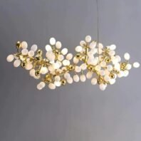 A contemporary horizontal chandelier featuring a cluster of white frosted glass orbs and golden accents. The fixture consists of numerous egg-shaped white glass globes arranged in an organic, branch-like formation. Interspersed among the white orbs are smaller, highly reflective golden spheres, adding a luxurious contrast. The structure supporting these elements is made of thin, gold-toned metal arms that branch out in various directions, creating a complex and intricate design. The overall shape of the chandelier is elongated and asymmetrical, resembling a stylized molecular structure or a modern interpretation of a flowering branch. Several of the white orbs are illuminated, emitting a soft, warm glow. The chandelier is suspended by thin wires against a neutral grey background, highlighting its intricate design and the interplay between the matte white glass and shiny gold elements.