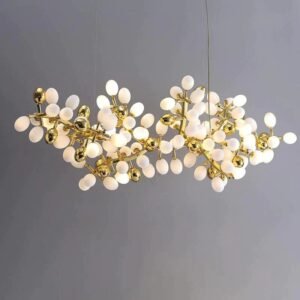 A contemporary horizontal chandelier featuring a cluster of white frosted glass orbs and golden accents. The fixture consists of numerous egg-shaped white glass globes arranged in an organic, branch-like formation. Interspersed among the white orbs are smaller, highly reflective golden spheres, adding a luxurious contrast. The structure supporting these elements is made of thin, gold-toned metal arms that branch out in various directions, creating a complex and intricate design. The overall shape of the chandelier is elongated and asymmetrical, resembling a stylized molecular structure or a modern interpretation of a flowering branch. Several of the white orbs are illuminated, emitting a soft, warm glow. The chandelier is suspended by thin wires against a neutral grey background, highlighting its intricate design and the interplay between the matte white glass and shiny gold elements.