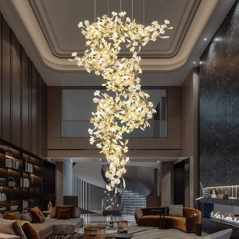 Breathtaking branch chandelier cascades through a two-story living area, featuring golden branches adorned with illuminated white floral elements. The chandelier's intricate design creates a stunning focal point, complementing the room's elegant decor. Set against a backdrop of warm neutral tones, dark marble accents, and plush furnishings, this exquisite branch chandelier adds a touch of organic luxury. Its soft, warm glow enhances the sophisticated ambiance, lighting up the space from the ornate ceiling to the modern seating area below. The chandelier's flowing form draws the eye upward, emphasizing the room's impressive height and architectural details.