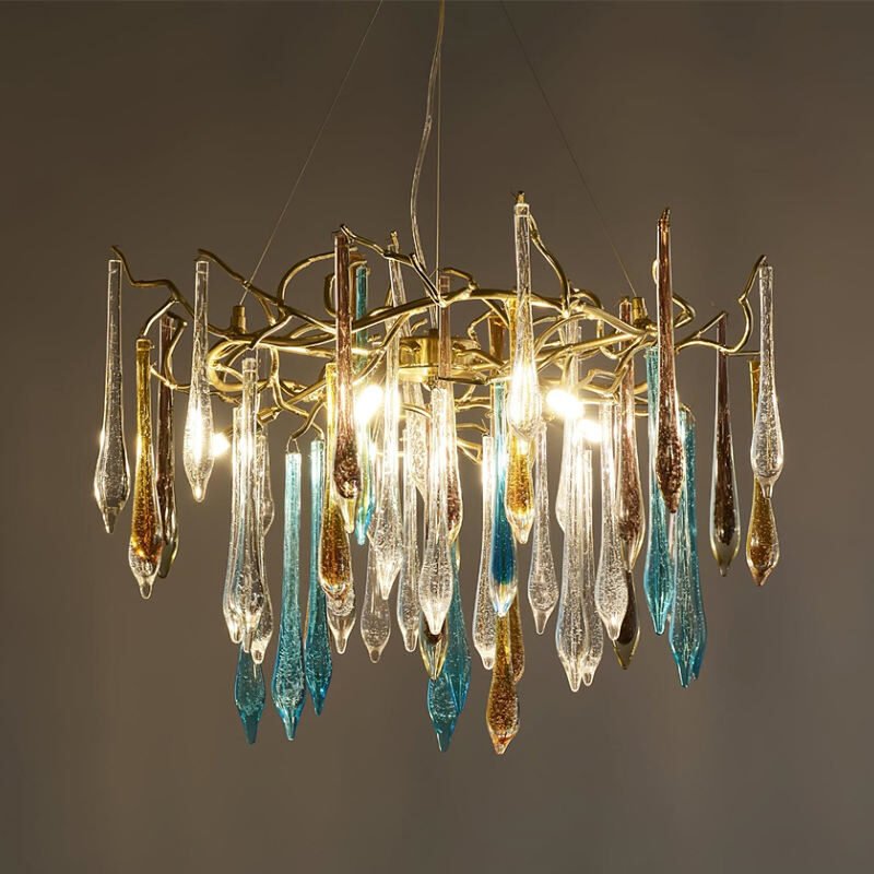 Ornate chandelier with golden branches supporting colorful glass icicles in clear, blue, and amber. Lit bulbs cast a warm glow through the textured glass droplets. The fixture hangs against a neutral background, showcasing its intricate design and luminous quality.