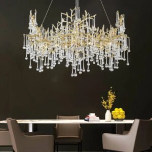 Modern dining room with a gold branch crystal chandelier as the centerpiece. The chandelier hangs above a white dining table, contrasting with dark walls. Intricate gold branches intertwine with crystal pendants, resembling a shimmering tree. Neutral-toned chairs surround the table. Decorative items on the table include a vase with yellow flowers, a bowl of lemons, books, and a coffee mug. The design balances luxury and minimalism, with the chandelier as the focal point. This setup showcases how statement lighting can transform a dining area into an elegant space.