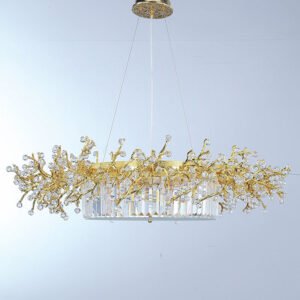 An elegant oval-shaped chandelier suspended against a light background. The fixture features a central oval base composed of vertically arranged crystal prisms, creating a luminous, curtain-like effect. Above this base, an intricate network of gold-plated branches extends outward, reminiscent of a golden coral reef or a stylized tree canopy. These branches are adorned with numerous faceted crystal orbs of varying sizes, resembling sparkling dewdrops or blossoms. The crystals catch and refract light brilliantly, adding a dazzling dimension to the piece. The gold branches create an organic, flowing silhouette that contrasts beautifully with the geometric precision of the crystal prism base. The chandelier is suspended by thin wires from a circular gold-toned ceiling mount with a textured, ornate design. The light background allows the intricate details of the chandelier to stand out clearly, emphasizing the interplay between the warm gold tones and the clear, sparkling crystals. This chandelier masterfully combines nature-inspired design with luxurious materials, resulting in a piece that is both a functional light source and an exquisite work of art. It would serve as a stunning focal point in any high-end interior space, particularly suited for dining areas or grand entryways.