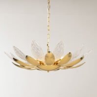 A elegant chandelier designed to resemble a blooming lotus flower, suspended against a light background. The fixture features alternating gold and crystal petals radiating outward from a central golden core. The gold petals have a smooth, ribbed surface with a warm metallic sheen, while the crystal petals are clear and intricately textured with a pattern reminiscent of delicate leaf veins. The crystal elements are transparent and catch light beautifully, creating a subtle sparkling effect. At the center, a golden orb forms the flower's core, from which the petals unfurl. The chandelier's base is a curved gold dish that supports the entire structure. Warm light emanates from within the chandelier, softly illuminating the petals. The piece is suspended by a delicate golden chain, adding to its refined appearance. This chandelier masterfully combines organic, lotus-inspired forms with luxurious materials, resulting in a striking blend of nature-inspired design and high-end aesthetics. It appears both delicate and substantial, promising to be a captivating focal point in any interior space.