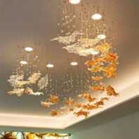 A spectacular large chandelier showcasing innovative custom lighting design for upscale hotels. This big chandelier features an array of golden and crystal-clear glass fish sculptures suspended at varying heights, creating a dynamic underwater scene. The hotel chandelier includes delicate wire suspensions with small crystal orbs, mimicking bubbles. Recessed spotlights complement the installation, while cove lighting enhances the room's ambiance. This exquisite custom lighting transforms the luxury hospitality space into an enchanting aquatic wonderland, demonstrating masterful craftsmanship and artistic vision.