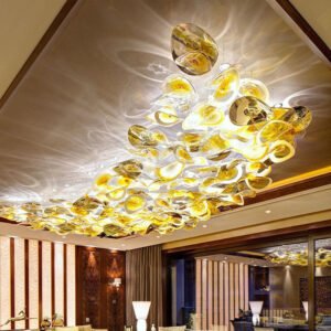 A spectacular large chandelier showcases innovative custom lighting design for luxury hotels. This big chandelier features a constellation of illuminated glass elements in warm golden hues, suspended from the ceiling in an organic, cloud-like formation. The hotel chandelier casts intricate light patterns on the ceiling, creating a mesmerizing interplay of light and shadow. Spanning the length of an elegant room with wood-paneled walls and modern decor, this unique lighting installation transforms the space into a captivating blend of artistry and illumination, perfectly elevating the sophisticated hospitality environment.