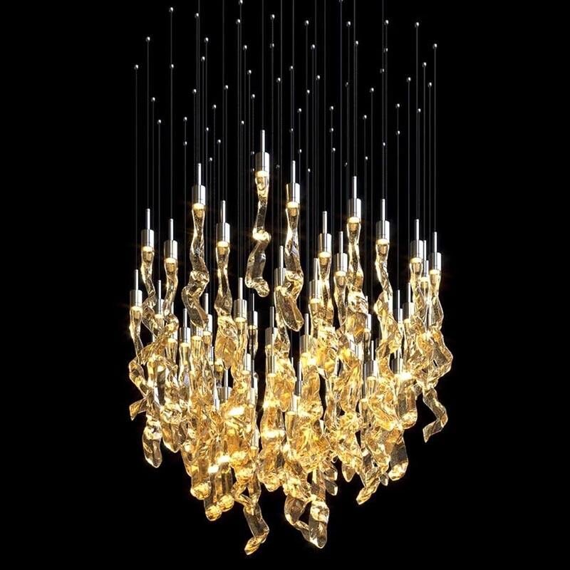 A magnificent large chandelier showcases innovative custom lighting design for luxury hotels. This big chandelier features a dense cluster of golden, organically-shaped glass elements suspended at varying lengths, creating a mesmerizing waterfall effect. Each piece glows warmly, resembling molten gold or amber crystals. Thin silver wires extend upward from the glass elements, topped with tiny LED lights, adding a starry canopy effect against the black background. This unique hotel chandelier transforms the space with its dynamic interplay of light and form, offering a stunning focal point that embodies both opulence and contemporary artistry.