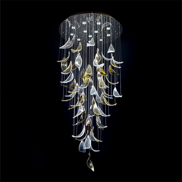 A magnificent large chandelier, ideal for luxury hotel lobbies. This big custom lighting fixture features a circular base with multiple small lights, from which thin wires suspend an array of glass elements. The glass pieces, resembling leaves or petals, cascade down in a mesmerizing waterfall effect. Clear and golden-hued glass forms intermingle, creating a dynamic play of light and shadow. The chandelier's elongated design draws the eye downward, culminating in a single golden leaf at the bottom. This bespoke lighting masterpiece exemplifies the artistry and innovation in custom lighting for grand, upscale spaces.