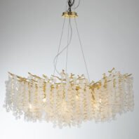 A luxurious oval-shaped chandelier featuring numerous crystal discs hanging from gold-toned branches. The chandelier is suspended from a gold circular base on the ceiling by thin wires. It emits a warm, golden glow, illuminating the textured crystal elements that create a cascading, waterfall-like effect. The fixture's design combines organic, branch-like structures in gold with delicate, transparent crystal discs, resulting in a harmonious blend of nature-inspired forms and refined elegance. The chandelier is photographed against a neutral light gray background, highlighting its intricate details and the interplay between the gold metalwork and the light-catching crystal elements.