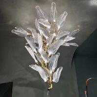 Exquisite branch chandelier featuring translucent glass leaves with intricate vein patterns. Golden branches support numerous illuminated leaf-shaped lights, creating a captivating botanical display. Each glass leaf glows softly, highlighting the delicate textures and organic forms. This stunning branch chandelier resembles a flourishing tree or shrub, its leaves arranged in a natural, asymmetrical pattern. The combination of ethereal glass and warm metallic accents adds depth and visual interest. Set against a dark background, the chandelier's radiant leaves stand out dramatically, showcasing the interplay of light and shadow. This nature-inspired lighting fixture serves as a breathtaking focal point, perfect for adding organic elegance to modern interiors.