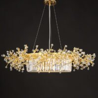 An elegant oval-shaped chandelier suspended against a dark background. The fixture features a central oval base made of vertically arranged crystal prisms, creating a luminous, curtain-like effect. Above this base, an intricate network of gold-plated branches extends outward, reminiscent of a golden coral reef or a stylized tree canopy. These branches are adorned with numerous faceted crystal orbs of varying sizes, resembling sparkling dewdrops or blossoms. The crystals catch and refract light brilliantly, adding a dazzling dimension to the piece. The gold branches create an organic, flowing silhouette that contrasts beautifully with the geometric precision of the crystal prism base. The chandelier is suspended by thin wires from a circular gold-toned ceiling mount. Light emanates from within the crystal prism base, illuminating the entire structure and emphasizing the interplay between the warm gold tones and the clear, sparkling crystals. This chandelier masterfully combines nature-inspired design with luxurious materials, resulting in a piece that is both a functional light source and an exquisite work of art. It would serve as a stunning focal point in any high-end interior space, particularly suited for dining areas or grand entryways.