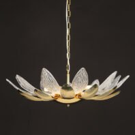 A stunning chandelier resembling an open lotus flower, suspended against a dark background. The fixture features alternating gold and crystal petals radiating outward from a central golden core. The gold petals have a smooth, ribbed surface with a warm metallic sheen, while the crystal petals are clear and intricately textured with a pattern reminiscent of delicate leaf veins. The crystal elements catch and refract light, creating a sparkling effect. At the center, a golden orb forms the flower's core, from which the petals unfurl. Warm light emanates from within the chandelier, illuminating the petals and creating a soft glow. The chandelier is suspended by a golden chain, adding to its luxurious appearance. This piece masterfully combines organic, lotus-inspired forms with luxurious materials, resulting in a striking blend of nature and high-end design. The chandelier appears both delicate and substantial, promising to be a captivating focal point in any interior space.