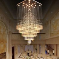 A breathtaking large chandelier dominates an opulent hotel lobby, exemplifying exquisite custom lighting design. This big chandelier features a square base with multiple lights, from which thousands of crystal strands cascade downward, forming a magnificent multi-tiered pyramid shape. The chandelier's warm, golden glow illuminates the cream-colored, ornately decorated room below, which includes elegant furnishings and classical architectural details. This unique hotel chandelier creates a stunning waterfall effect of light, transforming the lobby into a dazzling display of luxury and grandeur. It showcases how bespoke lighting can elevate high-end hospitality environments, creating an unforgettable first impression for guests.