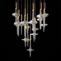 An innovative large hotel chandelier showcasing unique custom lighting design. This big chandelier features multiple glass elements resembling elongated spindles or hourglasses. Each piece consists of a clear, blown-glass center disc with tapered crystal extensions above and below. The glass components are suspended at varying heights by thin golden rods, creating a dynamic, cascading effect against a black background. The interplay of light on the crystal surfaces adds depth and sparkle to the design. This avant-garde piece exemplifies cutting-edge custom lighting, perfect for creating a striking focal point in modern, luxurious hotel spaces. The chandelier's unconventional form blends artistry with functionality, transforming the ambiance with its ethereal presence.