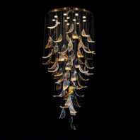 A stunning large chandelier, perfect for luxury hotel installations. This big custom lighting fixture features a cascading design of glass elements resembling petals or leaves. The chandelier's circular base is adorned with small lights, from which thin wires suspend numerous glass pieces. These translucent and golden-hued glass forms create a mesmerizing waterfall effect, descending in a graceful spiral. The interplay of light on the varied textures and colors of the glass elements produces a captivating, ethereal glow against the dark background, showcasing the artistry in bespoke lighting design for grand spaces.