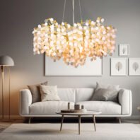 A contemporary living room featuring a striking crystal disc chandelier. The chandelier is composed of numerous white, clear, and gold-tinted crystal discs hanging from a gold-toned frame, creating a cloud-like formation. It's illuminated, casting a warm glow over the space. The room has a neutral color palette with light grey walls and a white sofa. Above the sofa, three framed botanical prints are displayed. To the left, a modern floor lamp with a dome shade adds to the lighting scheme. The room is furnished with a white modern sofa adorned with throw pillows, and a round coffee table with decorative items. The overall design is minimalist and elegant, with the chandelier serving as the focal point, adding a touch of luxury to the serene space.