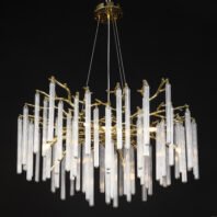 Opulent chandelier featuring numerous elongated glass tubes suspended from golden branches against a black background. The fixture hangs from a circular gold ceiling plate with an intricate textured design, supported by thin wires. The main body consists of organic, tree-like golden branches from which multiple clear, cylindrical glass pendants of varying lengths hang vertically. These glass elements have a ribbed texture, giving them a delicate, translucent appearance. The golden branches intertwine among the glass tubes, creating a natural, forest-like aesthetic. Warm light emanates from within, causing the glass tubes to glow brilliantly and creating a striking contrast against the dark backdrop. This chandelier exemplifies a blend of contemporary design with organic forms and luxurious materials, suitable for high-end interiors.