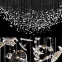 A large chandelier featuring custom lighting design with a multitude of suspended crystal elements. This big hotel chandelier creates a mesmerizing raindrop effect, with hundreds of crystal pieces in various shapes and sizes hanging at different lengths. The top image shows the full expanse of the chandelier against a dark background, resembling a sparkling cloud. The bottom image provides a close-up view, revealing intricate crystal shapes including discs, spheres, and organic forms. This spectacular custom lighting piece transforms spaces into magical, light-filled environments, perfect for creating an enchanting atmosphere in luxurious hotel lobbies or grand halls.