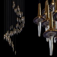 A stunning showcase of custom lighting design featuring a large hotel chandelier. The image presents two perspectives of the big chandelier: a distant view of its sweeping, curved silhouette on the left, and a close-up detail on the right. The chandelier comprises numerous glass teardrop pendants, each topped with a golden conical cap. The clear glass drops contrast beautifully with the gold accents against a black background. In the close-up, intricate details are visible, including the delicate glass shapes and the reflective qualities of the gold elements. This sophisticated piece exemplifies innovative custom lighting, perfect for creating a luxurious ambiance in high-end hotel spaces.