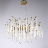 Elegant chandelier featuring numerous elongated glass tubes suspended from golden branches. The fixture is hung from a circular gold ceiling plate with an intricate textured design. The main body consists of organic, tree-like golden branches from which multiple clear, cylindrical glass pendants of varying lengths hang vertically. These glass elements have a ribbed texture, giving them a delicate, translucent appearance. The golden branches intertwine among the glass tubes, creating a natural, forest-like aesthetic. Soft light emanates from within, causing the glass tubes to glow and creating a ethereal effect. The chandelier is photographed against a neutral grey background, highlighting its unique blend of contemporary design with organic forms and luxurious materials.