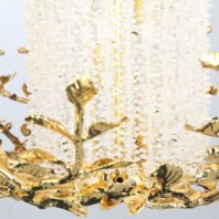 Close-up of a luxurious branch chandelier featuring cascading crystal beads and golden leaf-shaped ornaments. The chandelier's delicate crystal strands create a shimmering waterfall effect, contrasting beautifully with the intricate gold-plated branches and foliage. This elegant branch chandelier exemplifies opulent lighting design, blending nature-inspired elements with contemporary glamour.