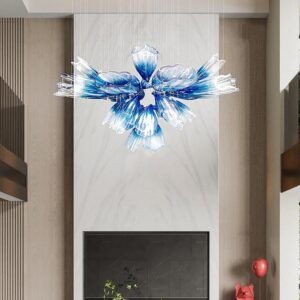 A striking custom lighting installation featuring a large chandelier composed of unique glass elements. This chandelier showcases an array of elongated, petal-like glass pieces arranged in a circular pattern, resembling a blooming flower. Each glass petal transitions from clear at the tip to a deep blue at the base, creating a stunning ombre effect. The custom lighting piece is suspended by thin wires in a modern interior setting with neutral tones. It hangs above a sleek fireplace, contrasting beautifully with the room's minimalist design. The chandelier's organic, fluid form and vibrant blue hues make it a captivating focal point, adding a touch of artistic elegance to the contemporary space.