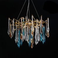 A stunning chandelier featuring a cluster of elongated glass droplets in various colors, predominantly clear, blue, and amber. The glass pieces resemble icicles or teardrops, each with a unique shape and internal texture. They hang from a complex network of gold-toned metal branches, creating an organic, tree-like structure. The chandelier is suspended by thin wires against a black background, which dramatically highlights the luminous quality of the glass and the intricate metalwork. This piece combines elements of nature-inspired design with modern artistry, resulting in a visually striking and elegant lighting fixture.