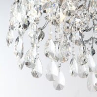 A close-up view of an exquisite crystal chandelier, showcasing the intricate details of its design. The image captures a section of the chandelier where multiple teardrop-shaped crystal pendants of varying sizes cascade downward. These crystal teardrops are faceted, allowing them to brilliantly refract light and create prismatic effects. Interspersed among the larger teardrops are smaller, round crystal beads and delicate silver-toned metal elements that resemble leaves or branches. The crystals are arranged in a layered, organic pattern, giving the impression of a crystalline waterfall or an elaborate ice formation. Light hitting the various crystal elements produces a dazzling display of sparkles and rainbow-like reflections. The background is a soft, light color, which allows the clarity and brilliance of the crystals to stand out prominently. This detailed view emphasizes the chandelier's luxurious craftsmanship and its ability to create a mesmerizing interplay of light and crystal, suggesting that the full fixture would be a stunning centerpiece in any elegant interior space.