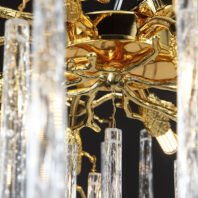 Close-up view of an opulent branch chandelier, showcasing intricate gold-plated metalwork resembling tree branches. The chandelier's central structure features a polished golden finish with ornate detailing. Delicate crystal pendants, shaped like elongated icicles, hang from the golden branches, creating a stunning contrast. The image captures the exquisite craftsmanship of the branch chandelier, highlighting the interplay between the warm, reflective gold surfaces and the sparkling, transparent crystal elements. This luxurious lighting fixture combines nature-inspired design with elegant materials, perfect for adding a touch of glamour to high-end interiors.