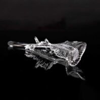 A close-up of a crystal fish skeleton, likely a component of a large custom lighting hotel chandelier. This intricate glass piece showcases remarkable detail, with clearly defined bones, fins, and skeletal structure. The transparent crystal gleams against a black background, highlighting its delicate craftsmanship. Such unique elements contribute to the overall design of big chandeliers, adding a touch of marine-inspired artistry to luxury hotel lighting installations.