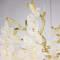 Detailed view of an elegant chandelier featuring gold-plated branches adorned with textured crystal discs. The image showcases the intricate design of the fixture, with polished gold-toned metal forming organic, tree-like branches. Hanging from these branches are numerous clear crystal elements, each with a unique, dimpled texture that resembles water droplets or ice crystals. The crystal discs are connected to the golden structure by thin, golden wires, creating a delicate and airy appearance. The combination of the reflective gold surface and the translucent, light-catching crystal elements creates a luxurious and sophisticated aesthetic. The chandelier is captured against a light background, emphasizing the contrast between the shimmering materials and the organic forms of the design.