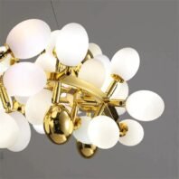 Close-up view of a contemporary chandelier featuring multiple round, white glass orbs attached to a golden frame. The chandelier consists of numerous frosted glass globes of varying sizes, creating a bubble-like appearance. These translucent spheres are illuminated from within, emitting a soft, warm glow. The structure supporting these glass orbs is made of polished gold-toned metal, with sleek arms extending outward to hold each globe. Interspersed among the white orbs are smaller, highly reflective golden spheres, adding a touch of luxury and contrast to the design. The chandelier is suspended by a thin wire, barely visible at the top of the image. Set against a neutral grey background, this lighting fixture combines modern minimalism with a playful, organic form, suitable for contemporary interior spaces.