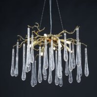 A stunning branch chandelier featuring a gold-toned, tree-like structure adorned with numerous clear crystal teardrop pendants. The intricate golden branches extend outward, supporting multiple elongated glass droplets that resemble icicles or raindrops. This elegant branch chandelier is suspended against a dark background, creating a dramatic contrast that highlights its luxurious design and delicate craftsmanship. The combination of organic, branch-like forms and sparkling crystal elements makes this chandelier a captivating focal point for any sophisticated interior.