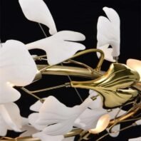 Close-up of a contemporary chandelier featuring delicate white glass petals and golden metallic branches. The chandelier's design mimics an abstract floral arrangement with organically shaped white glass pieces resembling flower petals or leaves. These translucent white elements are arranged around polished gold-toned metal structures that form the chandelier's core and branches. The gold parts have a smooth, reflective surface with curved and organic shapes, complementing the softer lines of the glass elements. Some of the white glass pieces appear to be illuminated from within, creating a soft, warm glow. The intricate interplay between the white glass and gold metal creates a striking contrast against the dark background, showcasing the chandelier's blend of natural inspiration and modern, luxurious design.