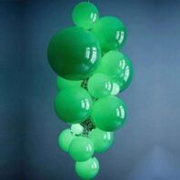 A striking custom lighting installation featuring a large hotel chandelier composed of multiple emerald green glass spheres. This big chandelier showcases an array of glossy, translucent orbs clustered together in varying sizes, creating a cascading bubble-like formation. The custom lighting piece is suspended against a deep blue background, creating a vivid color contrast. The green spheres emit a soft, ethereal glow, adding depth and luminosity to the design. This unique chandelier serves as a captivating focal point, perfect for adding a bold, modern touch to luxurious spaces while maintaining an organic, playful aesthetic.